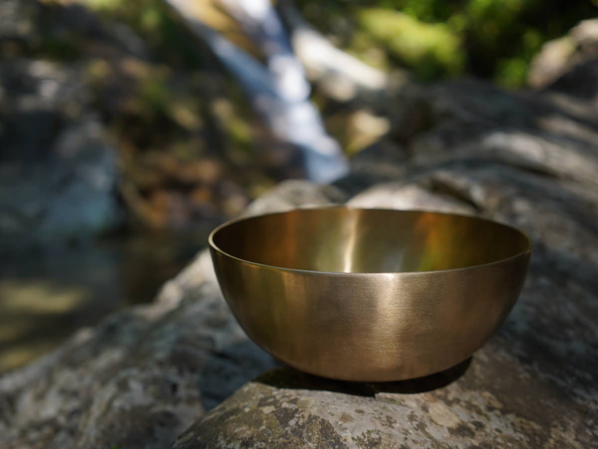 Bol chantant posé sur un rocher au bord d'une rivière et d'une cascade, symbole de calme et de vacances avant la reprise des massages sonores à Lausanne.
